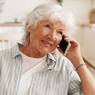 People, modern electronic gadgets, technology and communication. Aged senior woman with short gray hair enjoying nice phone conversation, sitting on sofa, holding mobile at her ear and smiling